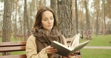 迷人的女人打开一本书，<strong>翻开</strong>白纸，然后开始阅读一本小说，而独自坐在秋天寒冷的公园里，穿着衣服